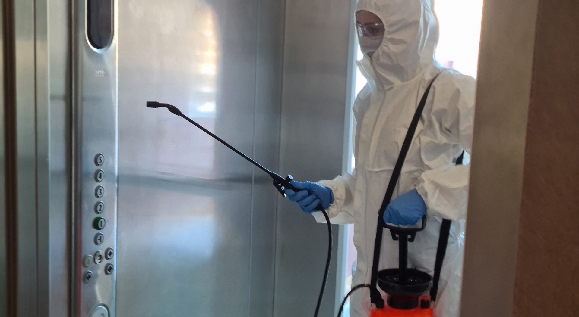 Coronavirus infection and flu paramedic in protective mask and suit disinfects elevator with spray bottle